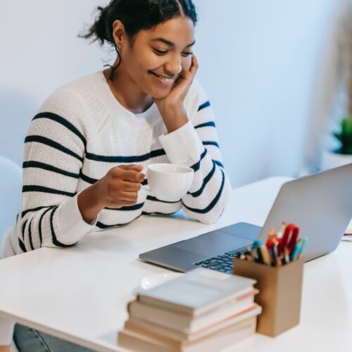 Young woman browsing the internet for books with a stack of books beside her.