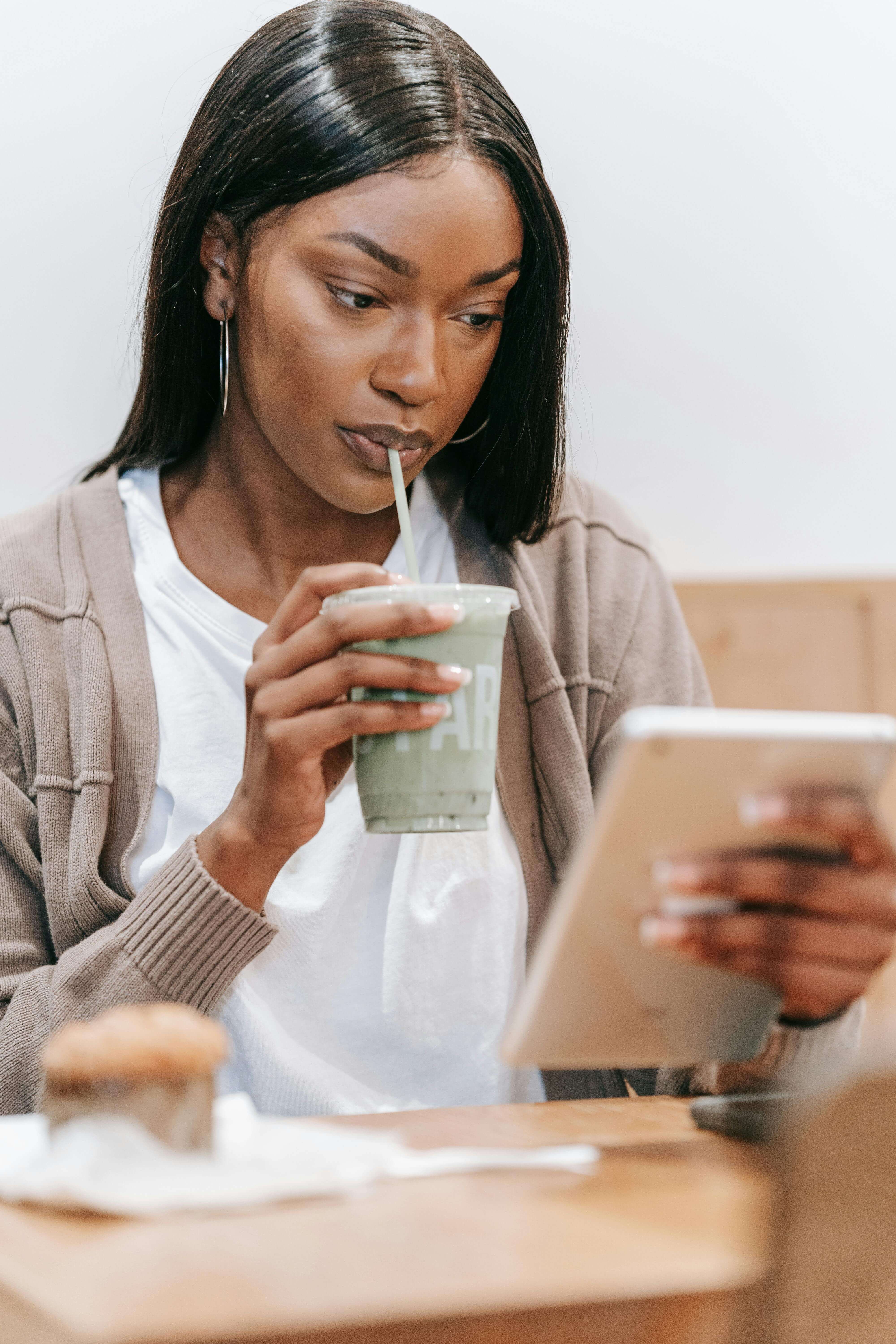 Black woman sipping a smoothie from a glass jar while relaxing at home, representing a calm, self-care morning routine.