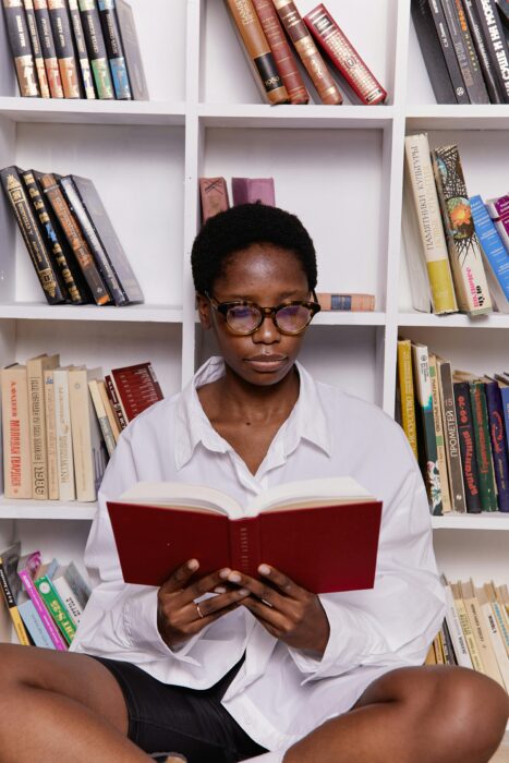 woman reading a book in front of white bookshelf
